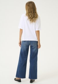 T-shirt blanc à manches courtes associé à un jean bleu à jambes larges. Le jean dispose de poches arrière et d'une coupe ample, accompagné de ballerines noires.