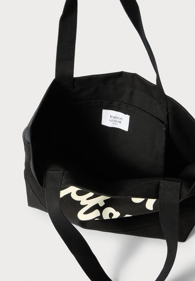 Must mustre kant, millel kreem logo trükiga. Omab vastupidavat kangast, topeltkandeid ja sildil sees on tekst "Maison Kitsuné Paris."
