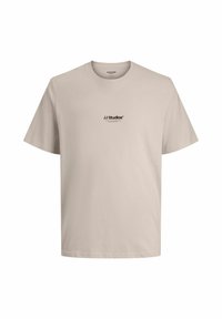 Camiseta de algodón beige con cuello redondo, mangas cortas y un pequeño logo negro que dice "JJ Studios" en el frente. Textura suave.