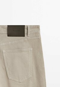 Pantalon en velours côtelé beige montrant la poche arrière et le patch en cuir marron foncé avec le texte « Massimo Dutti ».