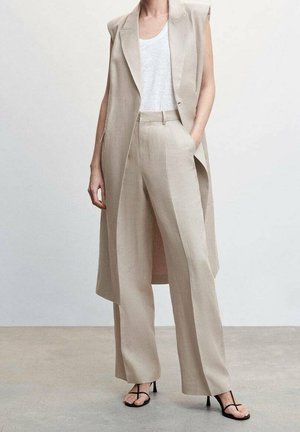 Beiger Dreiteiler-Anzug mit ärmellosem Blazer, Hosen mit weitem Bein und einfachem weißem T-Shirt. Sandalen mit dünnen schwarzen Riemen. Glatte Textur.