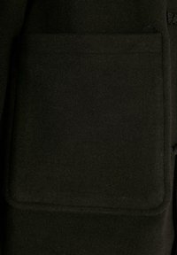 Section d'un manteau en laine noir avec une grande poche carrée, présentant une texture lisse et des bords nets, soulignant la douceur du tissu.