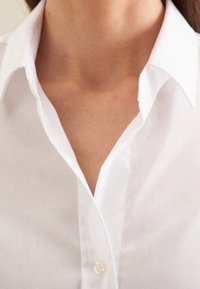 White collared shirt made of smooth fabric, featuring a buttoned placket and a classic collar design. Clean and minimal aesthetic.