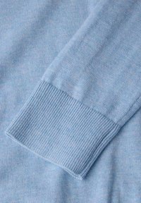 Ljusblått stickat tröjtyg med ribbad mudd, som har en mjuk textur och subtila färgvariationer. Närbild av ärmdetaljen.