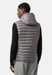 Gepolsterte graue Weste mit Kapuze, mit horizontalem Steppmuster und hohem Kragen, getragen über einem schwarzen Langarmtop und grauen Hosen.
