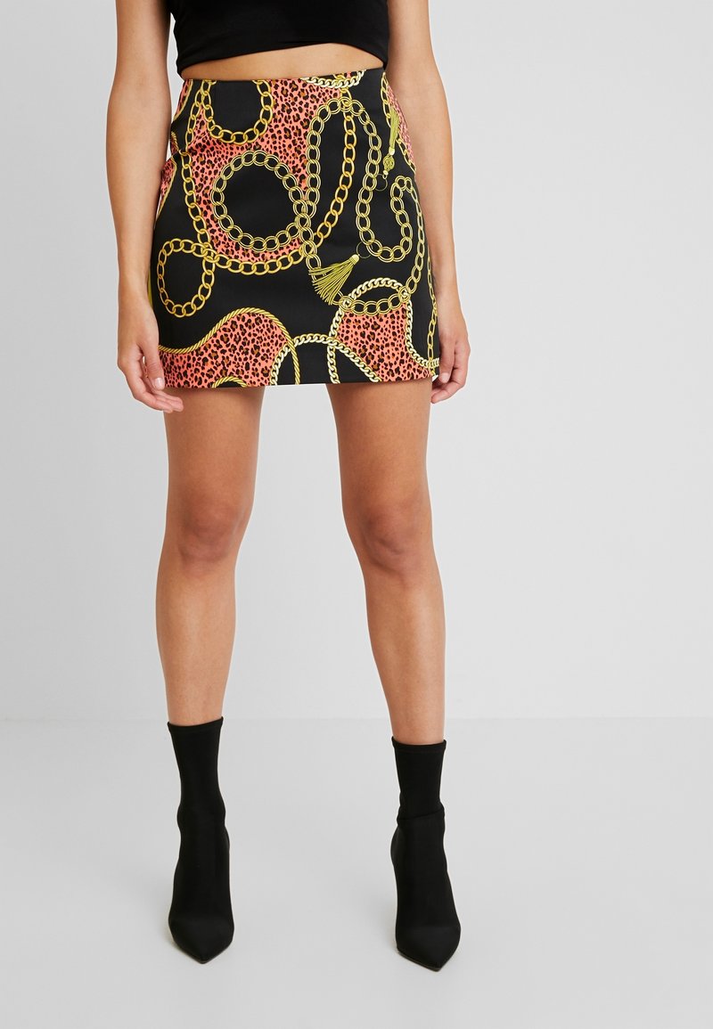 Mini-jupe noire avec un imprimé léopard rose et un motif de chaîne dorée. Portée avec des bottines noires, affichant une silhouette ajustée.