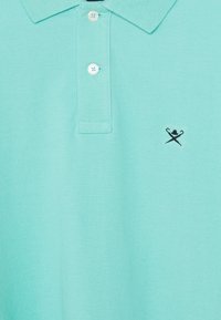 Ch polo turquoise en coton texturé avec une patte de boutonnage à trois boutons et un petit logo noir brodé sur la poitrine gauche.
