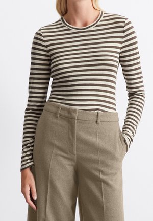 Kobieta ubrana w brązowo-biały, poziomo paskowany, długi rękaw wsunięty w beżowe, wysokiego stanu, dopasowane spodnie z kieszeniami.