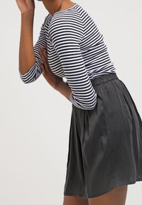 Randig långärmad topp i marinblått och vitt, ihop med svarta silkes kortbyxor. Skjortan har en figurnära design; kortbyxorna har ett elastiskt midjeband.