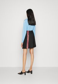 Top de manga larga azul claro con rayas blancas, combinado con una falda negra plisada que tiene rayas multicolores verticales a los lados. Sandalias de tacón negras.