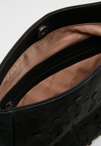 Bolso negro con diseño de corte en flores, con un exterior suave y un interior forrado de satén. Incluye un bolsillo con cremallera.