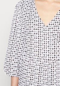 Vestido preto e branco aos quadrados com decote em V, mangas bufantes e detalhes florais bordados em um tecido leve. Cintura elástica franzida.