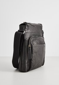 Bolso de cuero negro con un acabado texturizado, forma rectangular, múltiples compartimentos con cremallera y una correa de hombro de tela ajustable.