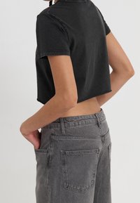 Camiseta negra cortada con mangas cortas, combinada con pantalones gris de cintura alta. Ambos tienen una textura suave y un diseño minimalista.