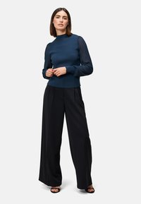 Mørkeblå sweater med ribbede lange ærmer, parret med sorte vide bukser. Glat tekstur og tætsiddende krop. Enkel, elegant design.