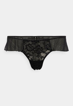Crna čipkana tanga s prozirnim panelima, cvjetnim uzorkom, nabranim rubovima i malim mašnom straga. Materijal izgleda mekano i delikatno.