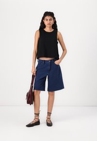 Svart ärmlös topp, lös passform. Blå denim bermudashorts, knälängd. Bruna platta skor med korsade remmar. Burgundy axelväska.