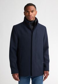Marineblauer Wollmantel mit hohem Kragen, ausgestattet mit einem Reißverschluss und zwei Seitentaschen. Glatte Textur mit kontrastierenden Knopfakzenten.