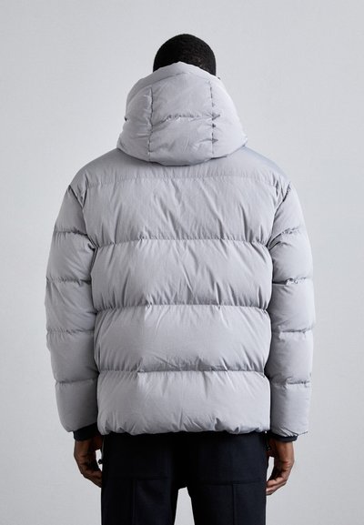 Jachetă puffer gri cu glugă, având secțiuni matlasate și o textură moale. Designul este voluminos, cu o croială lejeră.