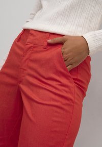 Rote Baumwollhosen mit geradem Schnitt, seitlichen Taschen und glatter Textur, kombiniert mit einem weißen gerippten Pullover.
