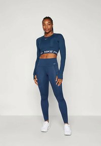 Συνδυασμός αθλητικής ένδυσης σε ναυτικό μπλε απόχρωση, που περιλαμβάνει ένα cropped τοπ μακρυμάνικο με λογότυπο στη μέση και κολάν ψηλόμεσα. Κατασκευασμένο από απαλό, ελαστικό ύφασμα.