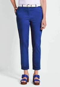 Blauwe op maat gemaakte broek met zijzakken, omgeslagen pijpen en een soepele textuur, gecombineerd met blauwe sandalen met houten hakken en een witte riem.
