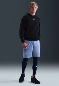 Sweat à capuche noir, shorts de sport bleu clair, leggings bleu marine et chaussures de sport noires. Logo Nike visible sur tous les articles.