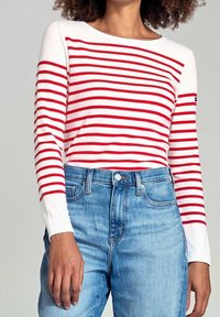 Gestreiftes Langarmshirt in rot und weiß mit rundem Ausschnitt, kombiniert mit hellblauen Jeans aus Denim. Weicher Stoff mit lässiger Passform.