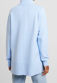 Suéter de punto de gran tamaño en azul claro con cuello alto, puños y dobladillo acanalados, y una costura central en la parte posterior. Textura suave.