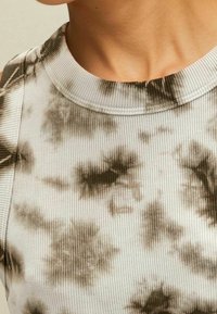 Ingrandimento di una persona che indossa un top senza maniche, a coste, con un motivo tie-dye in bianco e nero e un collo rotondo.