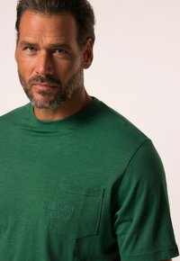 Camiseta de algodón verde con cuello redondo, que presenta un bolsillo en el lado izquierdo del pecho y texto en relieve "DENIM BRAND EST. 1880" en hilo a juego.