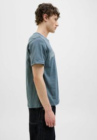 Fittet blå bomulds t-shirt med korte ærmer og rund hals, med en lysfarvet tekstprint på forsiden. Bruges sammen med mørke denimjeans.