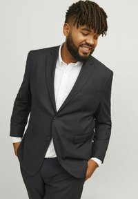 Un costume bleu marine foncé avec un blazer à un bouton et des revers crantés, accompagné d'une chemise blanche. Tissu lisse avec une coupe ajustée.