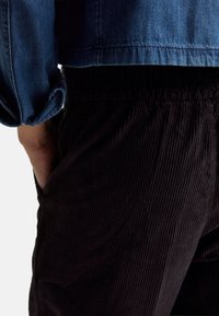 Tmavé manšestrové kalhoty s žebrovanou textura, v kombinaci s modrou džínovou bundou. Bunda má ohrnuté rukávy a zkrácený střih.