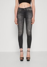 Black denim skinny jeans with distressed details and frayed hem, paired with black platform sandals and a cropped top.