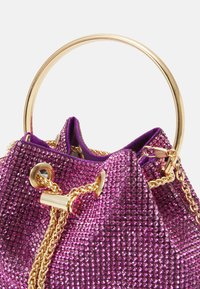 Violetti laukku, jonka pinnassa on tekstuuria ja rhinestone-koristeita, kultainen pyöreä kahva ja kultaketju. Sisus on vuorattu vastaavalla kankaalla.