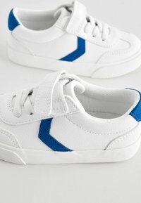 Baskets blanches en matériau synthétique texturé, avec des accents bleus et une bride Velcro, dotées d'une semelle en caoutchouc et de détails en lacets.