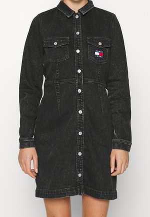 Schwarzes Jeanskleid mit langen Ärmeln, durchgehender Knopfleiste, zwei Brusttaschen und einem kleinen Logopatch. Wird mit einem leicht lockeren Sitz getragen.