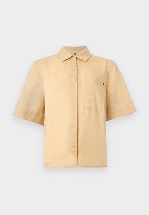 Μπεζ πουκάμισο με κοντά μανίκια, κουμπιά, γιακά και τσέπη στο στήθος, κατασκευασμένο από ελαφρύ ύφασμα σε απλό φόντο.