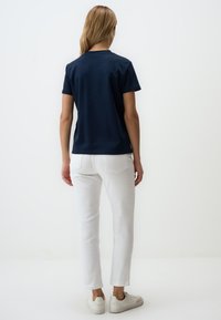 Camicetta blu navy a maniche corte abbinata a jeans bianchi e sneakers bianche. La camicia presenta un semplice scollo a girocollo e una texture morbida e liscia.