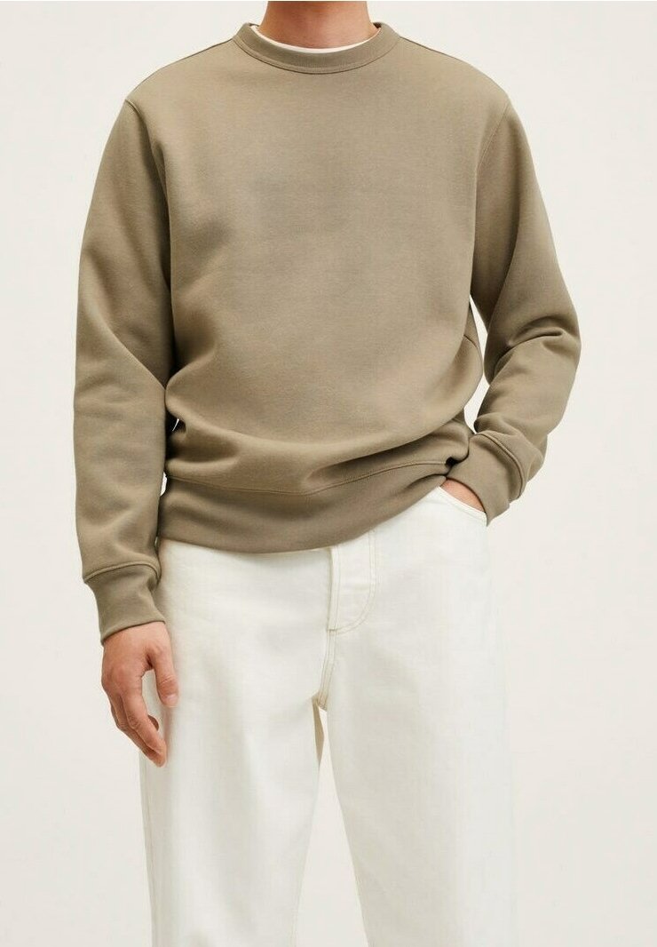 Uomo che indossa una felpa girocollo beige e pantaloni bianchi, con una mano in tasca e l'altra rilassata lungo il corpo.