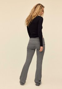 Schwarzes langärmeliges Oberteil kombiniert mit gestreiften Hosen mit weitem Bein, ausgestattet mit einer taillierten Passform und einem weichen, strukturierten Stoff.