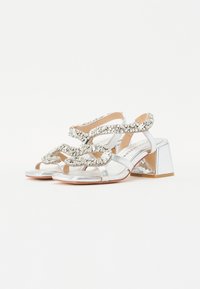 Sølvhelede sandaler med blokkheel, med en glitrende overflate, intrikate krystallpynt og åpen tå-design.