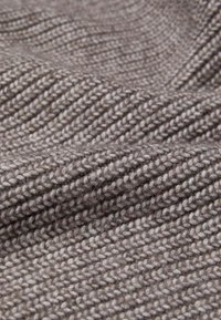 Strukturiertes, gestricktes Gewebe in einem sanften Grauton, mit einem gleichmäßigen Rippenmuster, sichtbaren Garn-Details und einer leicht flauschigen Oberfläche.