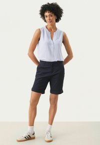 Ljusblå axelbandslös topp med V-ringning. Mörknavy rullade shorts. Vita sneakers med svarta ränder och vita strumpor. Enkelt, avslappnat design.