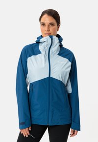 Giacca impermeabile blu con accenti azzurri, zip completa, cappuccio regolabile e tasche laterali. Presenta un mix di materiali lisci e testurizzati.