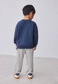Marineblauwe sweatshirt, gestreepte crème en marineblauwe broek, casual pasvorm. Witte sneakers met donkerblauwe accenten. Minimalistisch ontwerp en comfortabele textuur.