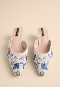 Broderade mules med en ljus creamfärgad ovandel, prydd med blommönster i blått, gult och grönt. Spetsig tå och öppen bakdel. Mjuk rosa innersula.