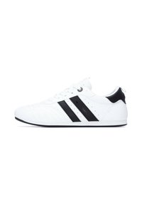 Zapatilla blanca con rayas negras, hecha de cuero suave, con detalles perforados, punta redonda y tapa de talón negra, suela plana.