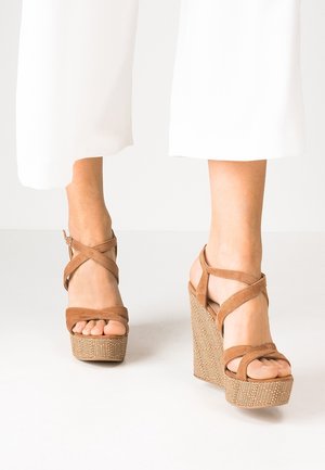 Braune Wildleder-Plateausandalen mit gekreuzten Riemen und geflochtenen Keilabsätzen, mit einem offenen Zehen-Design und strukturierten Details.